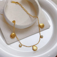 Gold shell charm bracelet flat lay on white plate